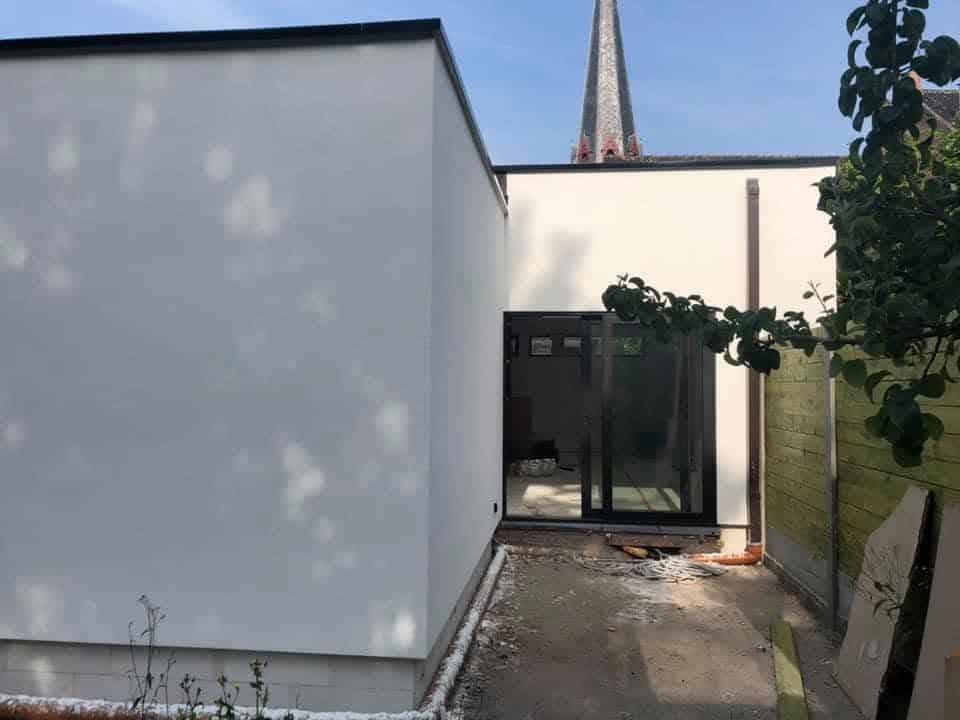 Detail van witte crepi gevelbepleistering naast een donker raamprofiel